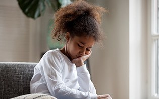 Child with toothache sitting on couch at home