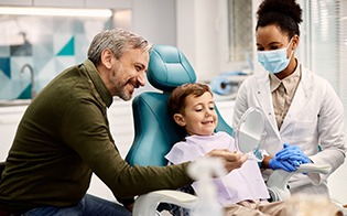 Child smiling at reflection with dentist and dad