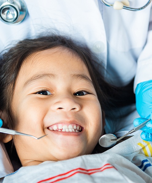 Little girl having her teeth examined with mom nearby